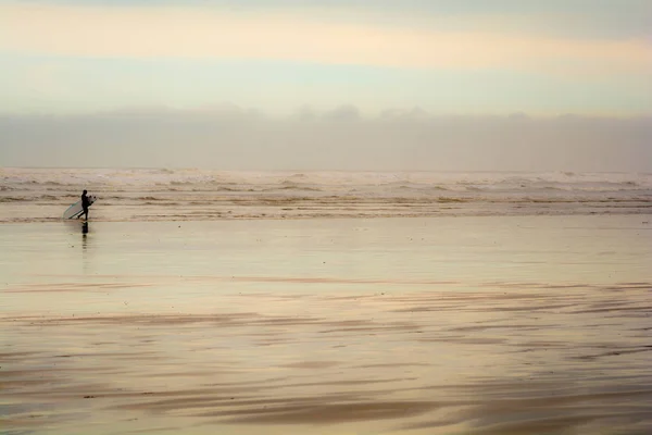 Un surfista lleva una tabla de surf en la costa de la playa —  Fotos de Stock
