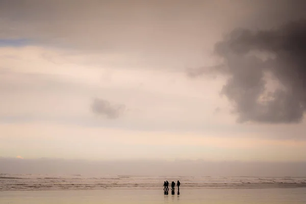 Grupo de personas caminando en una playa de arena con clima húmedo —  Fotos de Stock