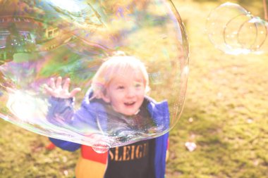 Çocuk gün içinde baloncuklarla bahçede oynuyor.