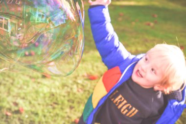 Çocuk gün içinde baloncuklarla bahçede oynuyor.