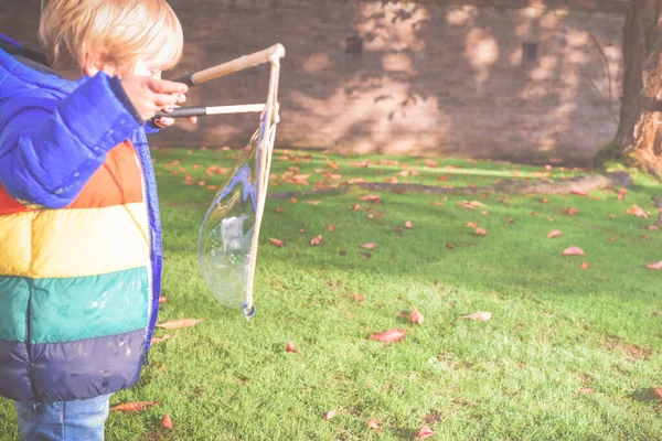 Ребенок играет на улице в саду в дневное время с пузырьками ч — стоковое фото