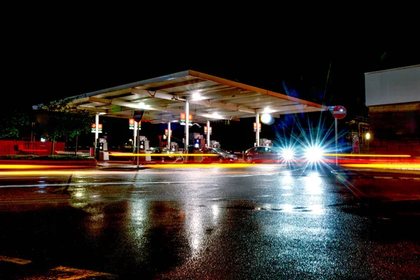 사람들 이 작업 할 때지나가는 차에서 나오는 불빛 이 밤에 주유소에 비치는 모습 — 스톡 사진