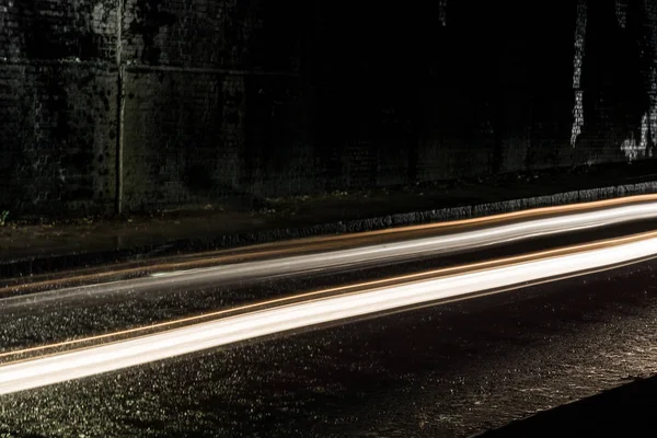 Trilhas de luz de carros que passam por um túnel escuro em um chuvoso — Fotografia de Stock