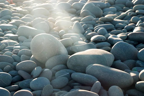 Een zonnestraal schijnt op een rots in een verzameling kiezelsteentjes — Stockfoto