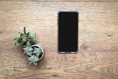 Mobile smart phone on wooden desk with blank screen and decorati