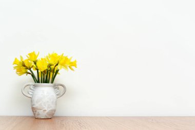 Kırsal bir vazoda çiçekler ahşap masa üzerinde beyaz iç duvar arka planı, nergisler