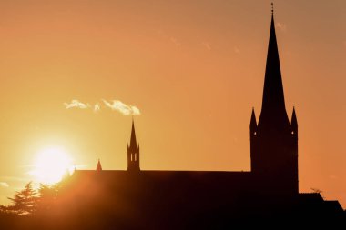 Gün doğumu ya da gün batımı siluetinde parlayan güneş ışığıyla kilise binası.
