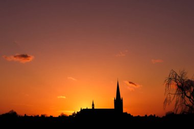 Gün doğumu ya da gün batımı siluetinde parlayan güneş ışığıyla kilise binası.
