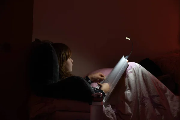 Girl reading a book in bed at night in comfy bedroom wearing pyjamas