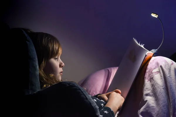 Girl reading a book in bed at night in comfy bedroom wearing pyjamas
