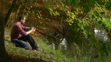 Adam açık havada bir yere oturmuş su Backpacker turist tarafından güneşli gün parkta sanal oyun oynamayı Video izlerken bir mesaj yazarak arama yapar gelir