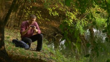 Adam açık havada su Backpacker turist tarafından güneşli gün parkta sanal oyun Video izlerken bir mesaj yazarak Video bir yerde oturan arar