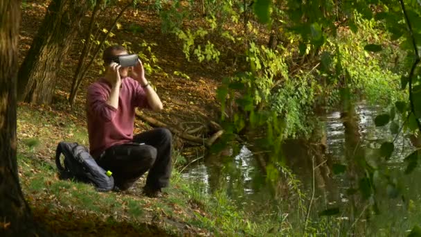 Man sätter på 360vr glasögon vaktande Video 360 grader håller en Smartphone känns spelet riktigt vrida huvudet spela virtuella spel i solig dag i parken — Stockvideo