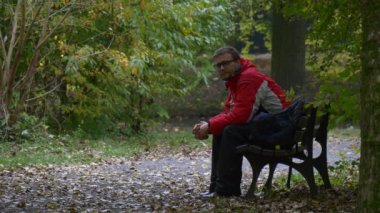 Spor ceketli ve gözlüklü bir turist bankta otururken bacaklarını esnetti ve sonbahar parkında yere düşen yapraklara baktı.
