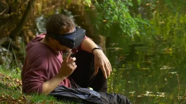 Człowiek w 360vr okulary włącza głowę zdejmuje słuchawki i kliknie telefon wpisuje wiadomość siedzi nad wodą, oglądanie wideo 360 stopni gra — Wideo stockowe