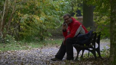 Turist sonbahar gün parkta bankta oturmuş ve kırmızı sportif ceket Backpacker Alley erkek ahşap Bank konuşuyor bir dinlenme açık havada olan arar