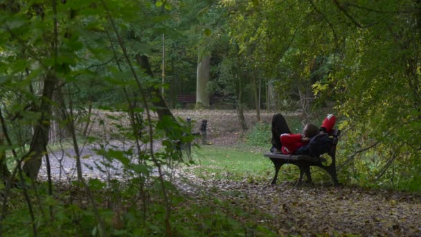 Young Man Lays on the Bench in Alley at Footpath Autumn Day Tourist With Backpack in Sporty Outfit Spends the Time in Forest Fallen Leaves on the Ground — Αρχείο Βίντεο