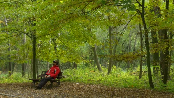 Człowiek w 360vr okulary siedzi pobiera się w Park jesienią oglądania wideo 360 stopni gry wirtualne gry toczenie jego głowy czuje się prawdziwej ławki gra w piłkę — Wideo stockowe