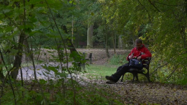 Man gaat zitten Put op 360vr bril kijken Video 360 graden virtuele spelen spelen in bewolkte dag Park Alley val Backpacker op verlaten houten bankje — Stockvideo