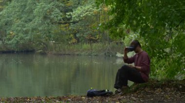 Adam tıklama telefon 360vr gözlük açık havada izlerken Video 360 derece Sanal oyunlar oynarken su bulutlu gün Park doğru nehir kıyısında yürürken koyar