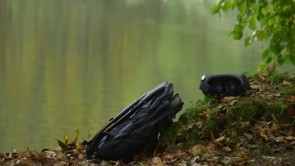 Un casque 360Vr et un sac à dos noir sont placés le long de la rivière Quelqu'un a regardé la vidéo 360 degrés jouant à des jeux virtuels dans le parc de jour nuageux au bord de l'eau — Video