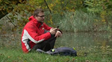 Adam cep telefonu sonbahar manzara oturan bir yerde sonbahar bulutlu gün yabani ördekler çoğu yüzme ile Lake yüzey su parkında mesaj atıyor