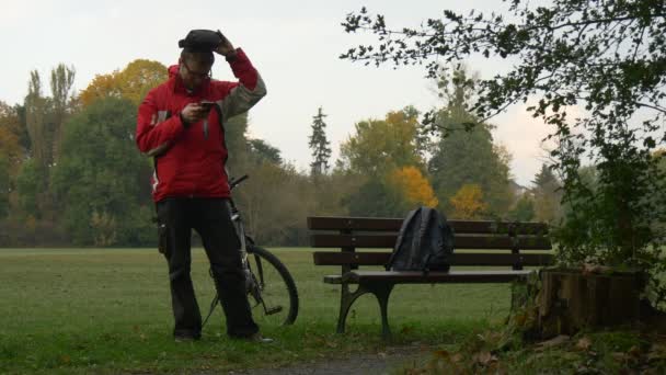 Mann im Park beobachtet die Virtual-Reality-Videobrille und steht an einem Herbsttag auf der Bank — Stockvideo