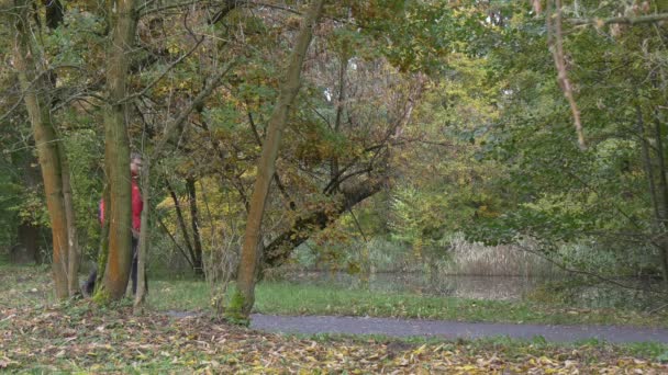 Человек делает селфи на фоне озера в парке. Осенний день облаков. в городском парке — стоковое видео