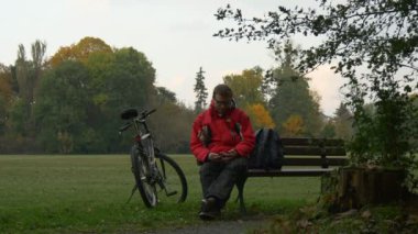 Turist bisikletçi yapar bir Video ara konuşurken oturan bulutlu sonbahar gün Bisiklet parkta bankta olduğunu sol arkasında tezgah bisikletçi Backpacker Park