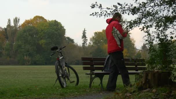 男人是使用手机发短信看视频 360 度玩虚拟游戏坐在公园的阴天秋天天背包客在公园长凳上 — 图库视频影像