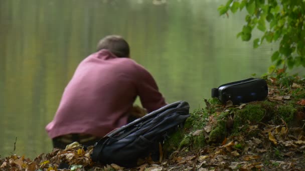 Man Clicks Mobile Phone Sitting on a Ground 360Vr Glasses Left on a Ground Outdoors Tourist Was Watching Video 360 Degrees Playing Games in Park by Water — ストック動画