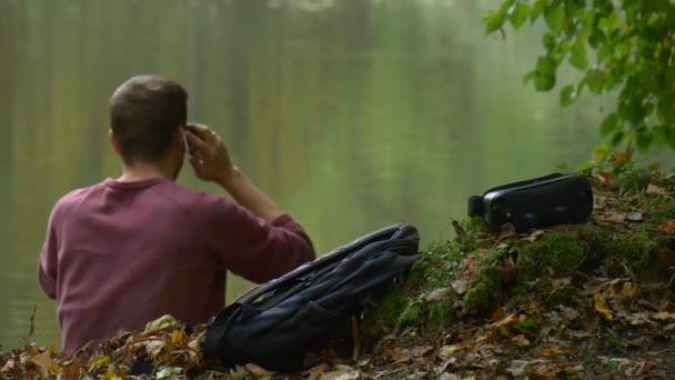 Homem se levanta para falar por telefone 360Vr óculos deixados em um solo ao ar livre Turista estava assistindo vídeo 360 graus jogando jogos virtuais no parque à beira da água — Vídeo de Stock