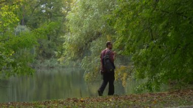 Backpacker oturur Gölü banka Park orman yürüme ve yumuşak su açık havada kuru yapraklar üzerinde bir yere sonbahar manzara dinlenme bakarak geliyor