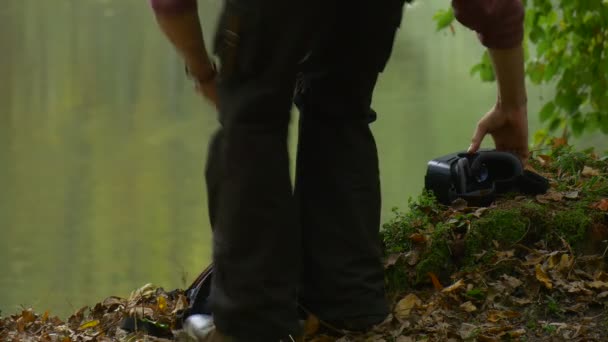 Tourist Comes Puts on 360Vr Glasses Lies Down Watching Video Using Smartphone Virtual Games Clicks the Device Man in Cloudy Autumn Day Park by the Water — Stock video