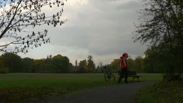Ποδηλάτη σε 360vr γυαλιά κάθεται βλέποντας βίντεο 360 βαθμούς παίζοντας εικονικά παιχνίδια που κάθεται στον πάγκο στο πάρκο ημέρα θολό φθινόπωρο απογειώνεται γυαλιά — Αρχείο Βίντεο