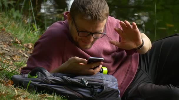 Turist tittar på skärmen på mobiltelefon leende videosamtal vaktande Video spela spel textilen klick smartphonen i soliga dag Park vid vattnet — Stockvideo