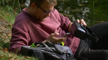 Biri 360vr kulaklık Tıklanma cep telefonu izlemek Video 360 derece oynarken sanal oyunlar yalan yere güneşli gün turist üzerinde Resting nehir göl