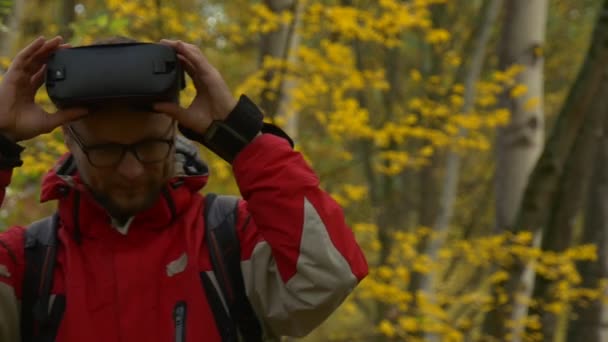 Man Comes se pone gafas de 360Vr viendo video 360 grados jugando de forma absorbente juegos virtuales girando la cabeza en el parque de día nublado en otoño hojas amarillas — Vídeo de stock