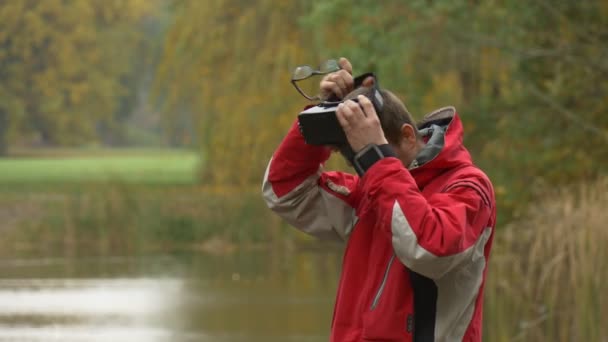 Τουριστικές παίρνει μακριά γυαλιά βάζει vr γυαλιά κατά την λίμνη τράπεζα βλέποντας βίντεο 360 βαθμούς παίζοντας παιχνίδια τεντωμένο χέρι του συννεφιασμένος ημέρα πάρκο το φθινόπωρο — Αρχείο Βίντεο