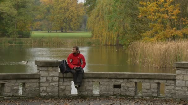 Tourist nimmt 360vr Brille ab, sitzt auf Brücke über den See und schaut 360-Grad-Video an, spielt Spiele und ruht sich am Wochenende aus — Stockvideo