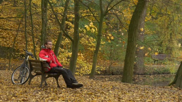 Touriste Vue sur le lac met sur 360Vr lunettes assis sur un banc dans le parc Regarder la vidéo 360 degrés Jouer à des jeux Automne Paysage Cycliste dans le parc — Video