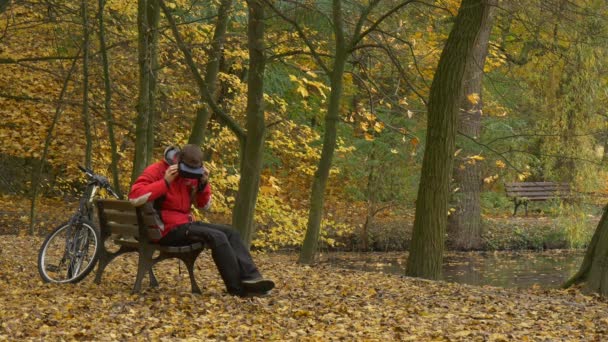 Man in 360Vr Headset Turning Head Senta-se no banco no parque Obtém-se assistindo vídeo 360 graus Jogos de reprodução Sinta o vídeo Real Resting at Autumn Landscape — Vídeo de Stock