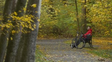 Sokak sonbahar gün Backpacker ve yere eğildi geri sonra onun dirsek sarı yaprakları Park adam altın ağaçları arasında bir bankta oturan bisikletçi