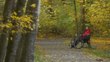 Sokak sonbahar gün Backpacker ve yere eğildi geri sonra onun dirsek sarı yaprakları Park adam altın ağaçları arasında bir bankta oturan bisikletçi