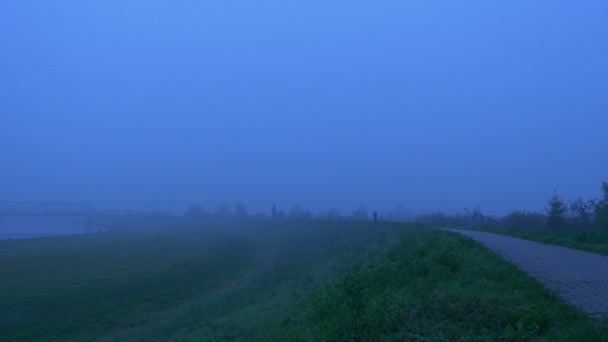 Mensen silhouetten lopen naar elkaar mistige ochtend toeristen Backpackers gaan om elkaar te ontmoeten door de rivier herfst dag wandelpad langs groen gazon — Stockvideo