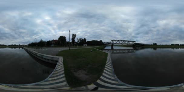 360Vr видео железнодорожный мост через реку Одер пирс Здания Одер гладкая вода Пейзаж на закате облака Зеленая лужайка съемки в течение синего часа вечером — стоковое видео