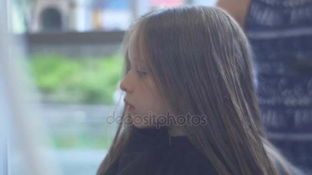 Parrucchiere pettini e asciuga i capelli dei bambini parrucchiere parrucchiere Stylist sta facendo un taglio di capelli taglio di capelli bambina è seduta con il viso serio in Peignoir — Video Stock