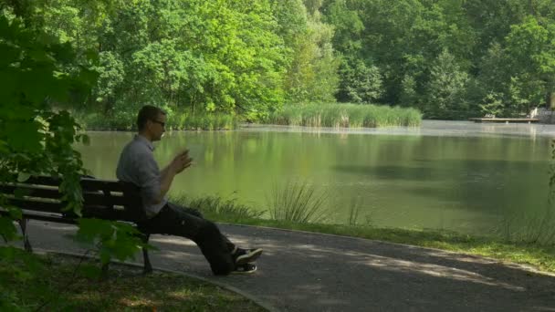 Turista sentado en el banco con Tablet Virtual Negocios Forex Trading Pago en línea Pedidos a través de Internet Turista en el parque junto al lago Fresco soleado verano — Vídeos de Stock