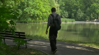 Park Lake turist arasında taze yeşil ağaçlar güneşli bahar gün yumuşak su Asfaltlı patika ahşap Bank tarafından tezgah ayakta kalan adam geliyor