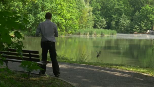 Hombre viene a descansar en el parque mirando patos salvajes se sienta en el banco junto al lago árboles verdes soleados Primavera de Europa turista de agua suave en banco de madera — Vídeos de Stock